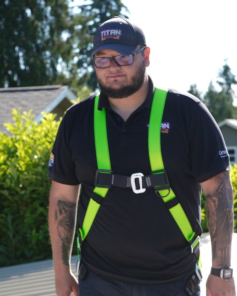 Gil Matos, owner of Titan Roofing, standing on a roof in a Titan cap and safety harness