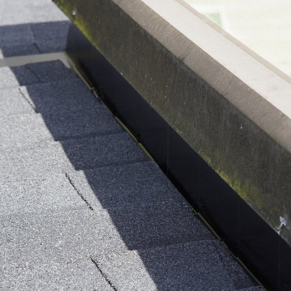 Metal flashing sealing the edge of a skylight where it meets new asphalt shingles