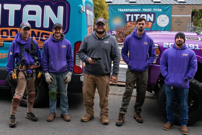 Five members of the Titan Roofing crew in Titan hoodies standing in front of the Titan van and truck
